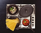 Stainless steel hob with boiling pasta water, fish in a pan, tomato sauce and stew pot