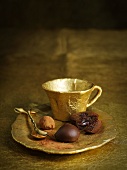 A gold coffee cup with filled chocolates on the saucer