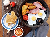 English breakfast with fried eggs, bacon, small sausages, baked beans and toast