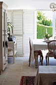 Rustic Rococo style - dining area in front of terrace door with view of garden and white folding window shutters