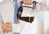 Mann giesst Kaffee aus Kanne in einen Becher