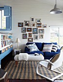 Cheerful blue and white living room below sloping ceiling; collection of photos in vintage picture frames above couch