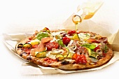 Olivenöl auf Pizza mit Gemüse und Schinken gießen