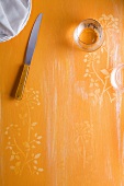 An orange surface with a flower pattern, a knife, stacked plates and a glass