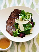 Steak Served with Salad with Shaved Parmesan Cheese; On a White Plate