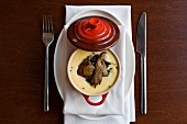 Mushroom Polenta with Shiitake Mushrooms in a Red Creuset Ramekin on a White Napkin with Fork and Knife