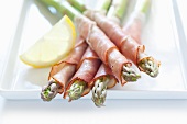 Asparagus wrapped in ham, with lemon, on a tray