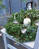 Winter wreath of juniper with Christmas-tree-shaped decorations and candle on terrace