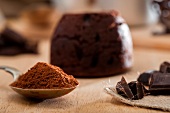Schokoladenkuchen mit flüssigem Kern; davor Kakaopulver und Schokoladenstücke