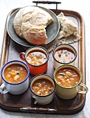 Several mugs of soup and white bread on a wooden tray