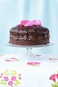 A chocolate layer cake topped with rose petals, on a cake stand