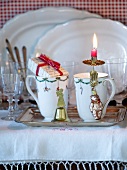 Mugs with Christmas decorations on silver tray in front of glasses and white porcelain dishes