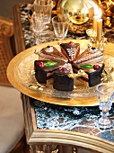 Ornamental cake slices on a brass tray next to crystal glasses on an antique table with a stone top