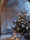 Dekorierter Weihnachtsbaum mit brennenden Kerzen vor modernem Stuhl aus transparentem Kunststoff mit Engeln dekoriert