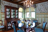 Antique dining table and chairs with elegant upholstery in front of display cabinet against painted wood panelling in traditional dining room