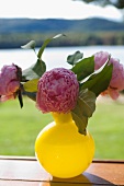 Rosa Pfingstrosen in gelber Vase auf Holzunterlage