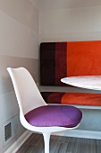 White plastic shell chair with purple cushion in front of bench with striped upholstery