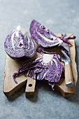 A red cabbage, cut into pieces, on a chopping board with a knife
