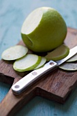 A Granny Smith apple with some cut slices on a chopping board