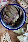 A cooked artichoke in a bowl with bread (view from above)