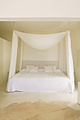 Puristischer Schlafplatz mit konvex drapiertem Stoffbaldachin und seitlichen Vorhängen in kahlem Raum
