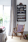 Garden deckchair below toys on wall-mounted shelves and foot of bed in front of French windows