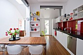 Bouquet of tulips on dining table in modern, open-plan kitchen with long kitchen counter and red glass splashback