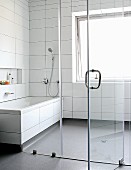 Bathroom with white tiles and grey plastic flooring separated by glass wall
