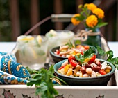 Bowls of Bean and Tomato Salad with Feta Cheese on a Tray with Drinks on an Outdoor Table