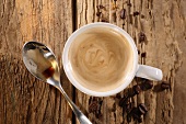 A cup of espresso with a spoon and coffee beans on a wooden surface