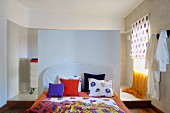 Floral-patterned linens on bed against half-height partition screening ensuite bathroom