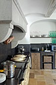 Vintage Küchenzeile mit Arbeitsplatte und Spritzschutz aus schwarzem Stein unter gemauertem Abzug in ländlicher Küche mit Rundbogen Wandnische
