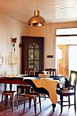 Antique chairs and metal stools around a dining table covered with an cowhide rug; china hutch in front of a wood paneled wall