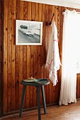Dreibein vor holzverkleideter Wand mit Fotografie und Tuch an Garderobenhaken