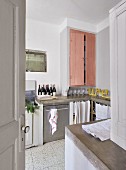 View though open door of kitchen counter and fitted cupboard with pink doors in simple interior