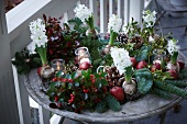 Weihnachtsgesteck aus Tannenzweigen, Scheinbeeren, Lorbeer, Äpfeln, Misteln, Hyazinthen und Pinienzapfen mit Windlicht auf dem Terrassentisch