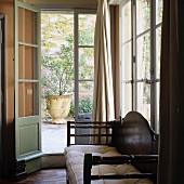 Antique wooden bench with seat cushions in window niche with door leading to Mediterranean terrace