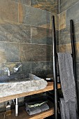 Rustic stone wash basin on wooden counter with ladder-like towel rack leaning on wall in corner of bathroom with marbled stone tiles