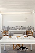 Gemauertes Sofa mit Kissen und Tische mit Regiestühlen auf überdachter Terrasse