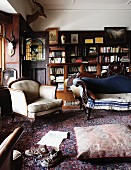 Heller, antiker Polstersessel und geschwungene Sitzbank mit blauem Bezug auf Orientteppich vor Bücherschrank im Wohnzimmer