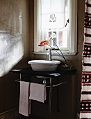 Vase mit Anthurien auf kleinen Waschtisch mit Metallgestell und weisser Waschschüssel vor Fenster in schlichtem Ambiente
