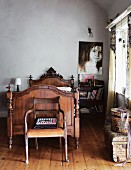 Antique wooden chair in front of a carved, wooden sleigh bed and modern portrait painting on the wall in a no frills room