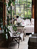 Cozy corner of a country home veranda - rattan chair and rustic wooden table with peeling paint next to a day bed along a stained glass wall