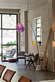 Kleiner Tisch mit Stühlen im Retrostil und Stehlampe mit flippig violettem Schirm vor raumhoher Fensterfront im Loft