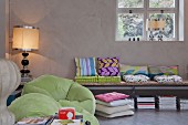 Collection of colourful cushions on wall-mounted bench, lime green beanbag chairs and postmodern table lamps contrasting with cool exposed concrete of loft interior