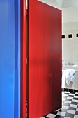 Blick durch rote, offene Tür ins Bad mit schwarz-weißem Schachbrettboden
