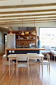 Modern, Scandinavian-style dining area in front of open-plan kitchen with woman behind counter