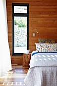 Double bed against wood-clad wall next to window