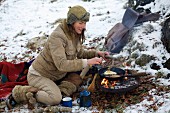 A woman frying an egg and bacon outdoors