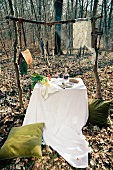 A table laid outdoors with vegetables and a tablecloth; in addition, there are fish hanging from a rustic wooden frame